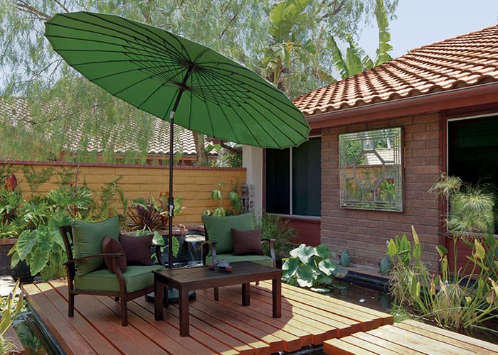 green parasol style umbrella over matching green patio seating on a wooden deck