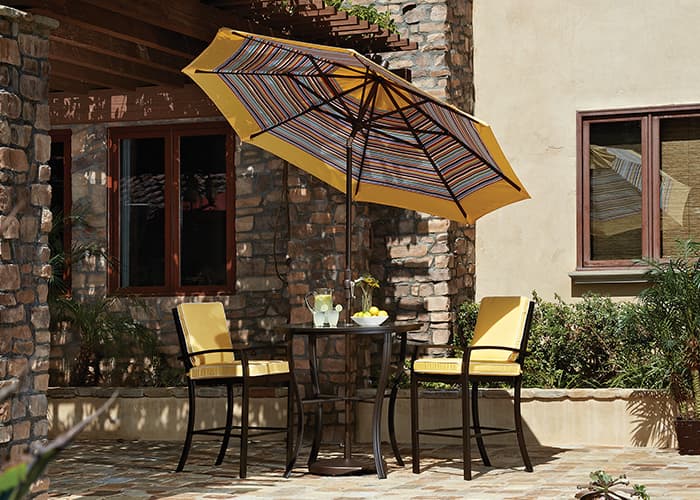 small striped yellow umbrella shading a bistro set on a sunny stone patio