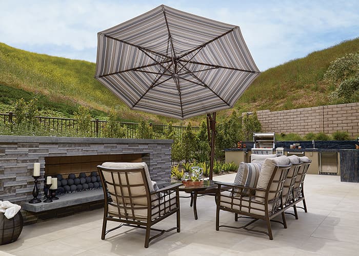 grey striped medium cantilever umbrella over a small patio conversation set with green hills surrounding it